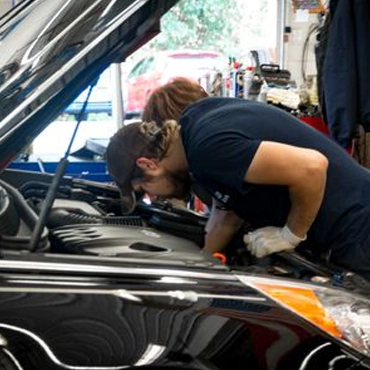 Mechanic leaning over an open car hood, inspecting the engine in a busy garage.