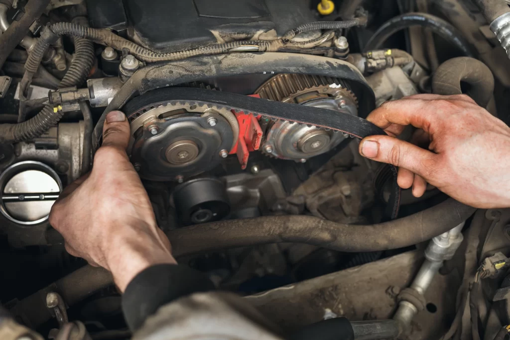 Hands working on a car engine, adjusting a timing belt around gears and pulleys.